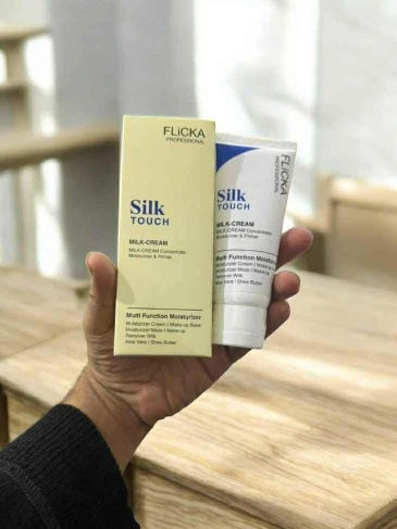 Hand holding Flicka Silk Touch milk cream packaging and tube on a wooden surface.