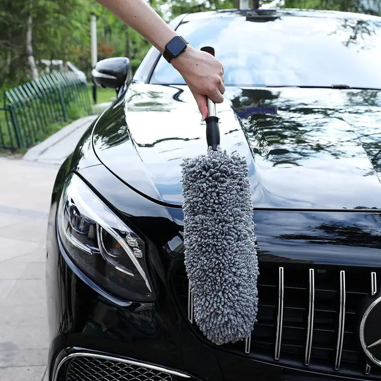 Person cleaning a black car with a gray microfiber duster.