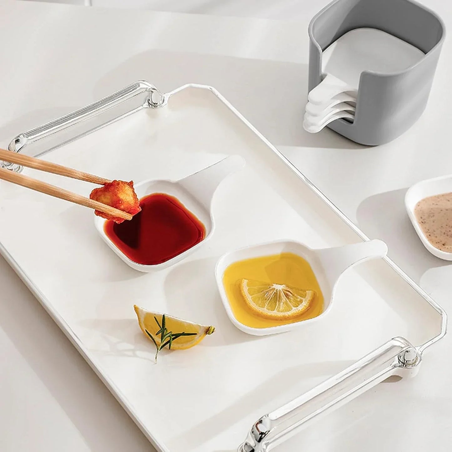 White tray with compartments containing red and yellow sauces, a lemon wedge, and chopsticks dipping into the red sauce.