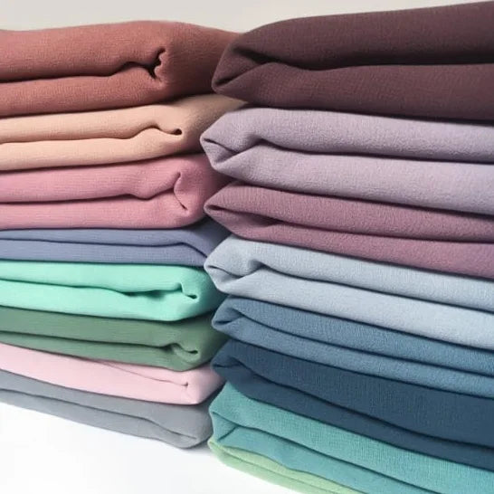 Stack of folded fabric in various pastel colors on a white background