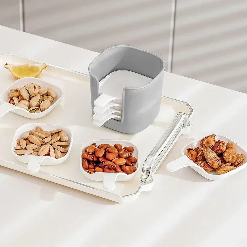 Set of small white bowls with different types of nuts on a tray, with a gray container in the center.